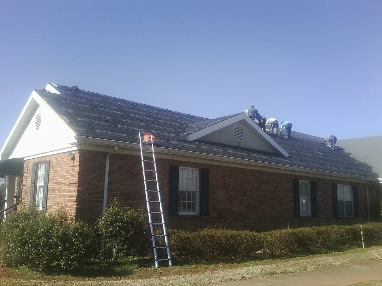 Crew tearing shingles off a brick ranch roof with a ladder set — Emergency Roof Repair work by our crew in Glendora