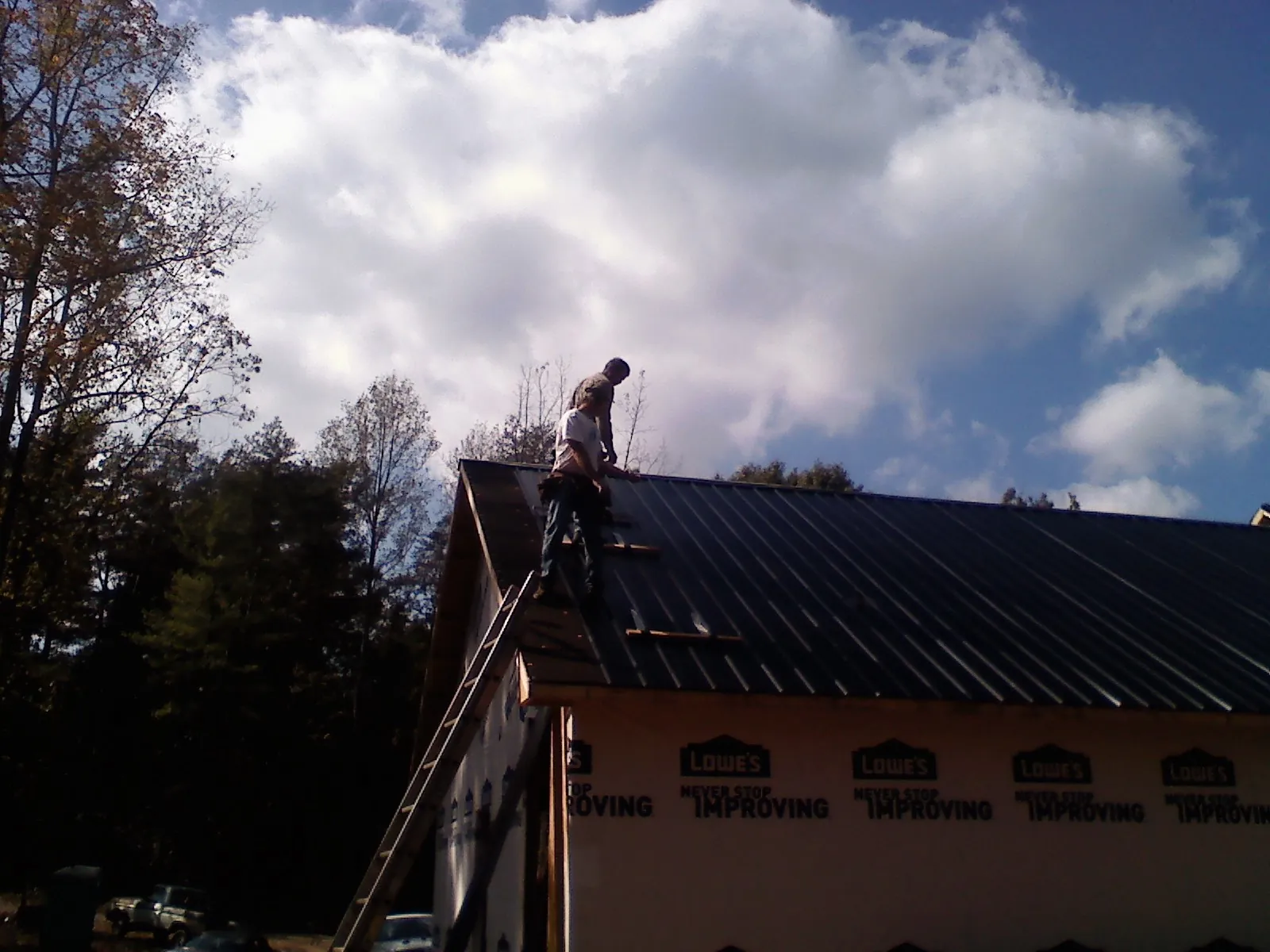 Roofer fastening dark metal panels high against a cloudy sky, from a Roof Inspection job in Glendora